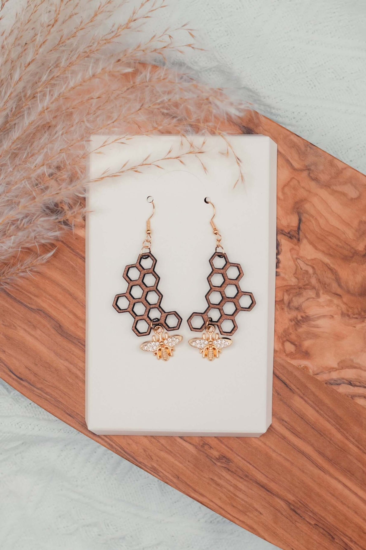 Honeycomb Bee Earrings with wooden honeycomb design and gold-plated rhinestone bee charm displayed on a wooden board.