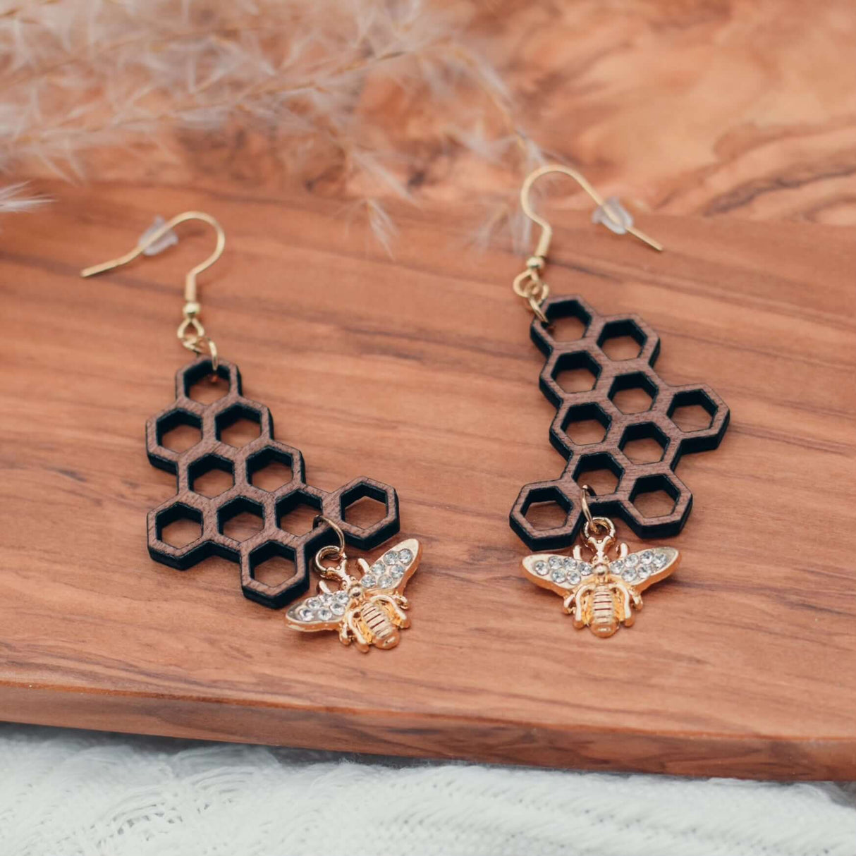 Handcrafted Honeycomb Bee Earrings with dark walnut honeycomb design and gold-plated rhinestone bee charm, displayed on wooden surface.