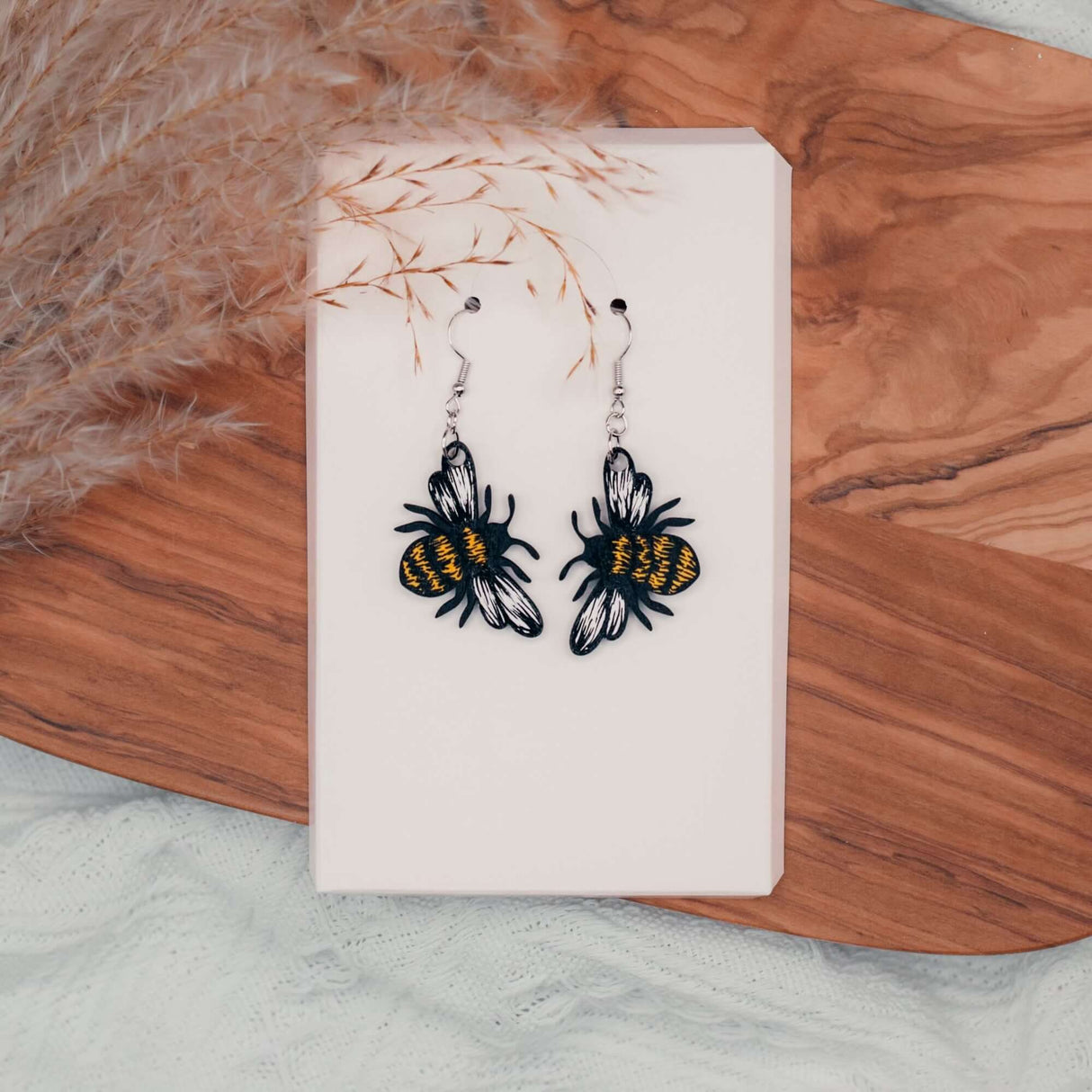 Handpainted Bumblebee Earrings on white background with wooden plank and dried flowers