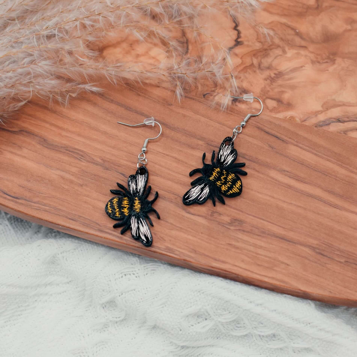 Hand-painted bumblebee earrings with vibrant black and yellow design on wooden surface