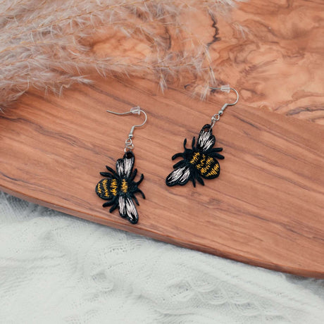 Hand-painted bumblebee earrings on wooden surface with natural accents.