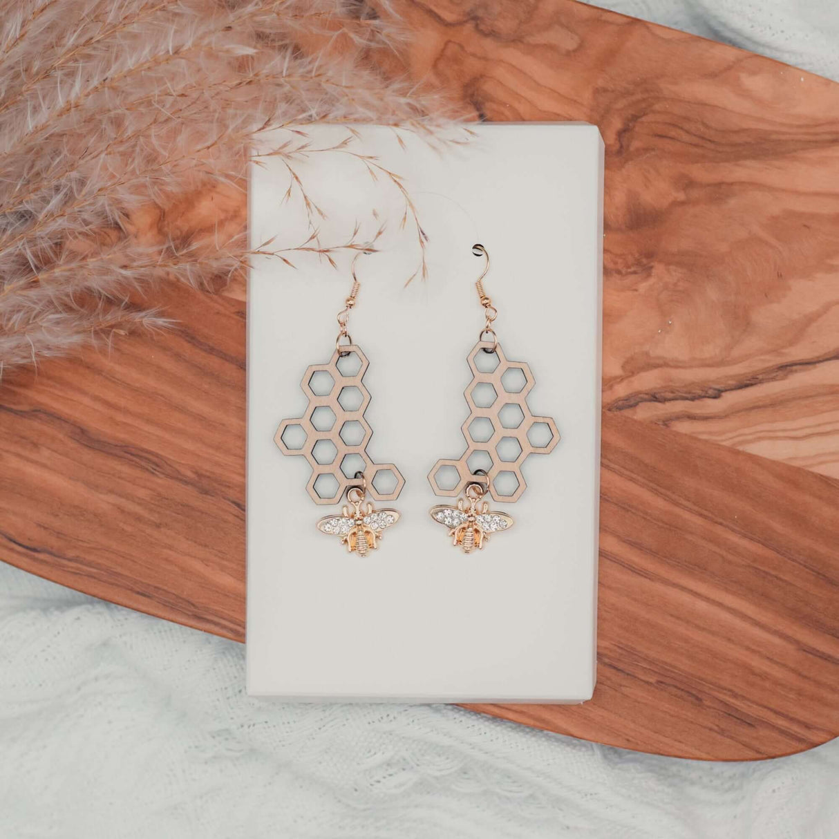 Honeycomb Bee Earrings with gold-plated rhinestone bee charm on wooden background.