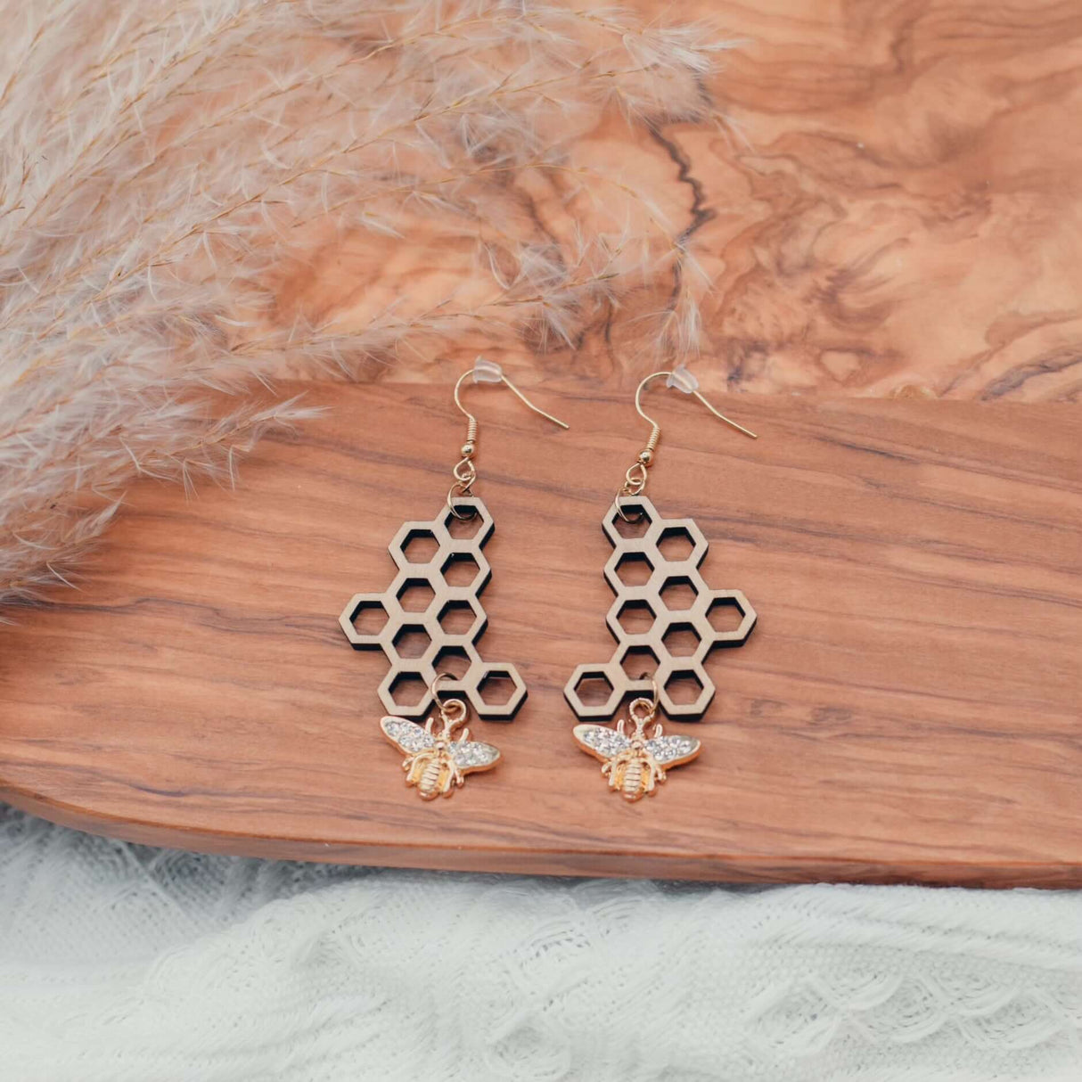 Handcrafted honeycomb bee earrings with gold-plated bee charm on wooden surface, featuring intricate design and natural elegance.