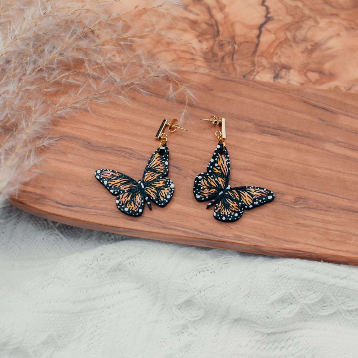 Hand-painted wooden butterfly earrings on wooden surface, showcasing vibrant colors and delicate craftsmanship.