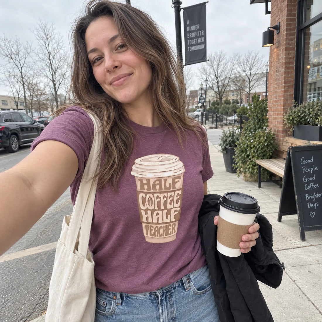 A woman takes a selfie outdoors wearing a heathered purple graphic t-shirt that reads &