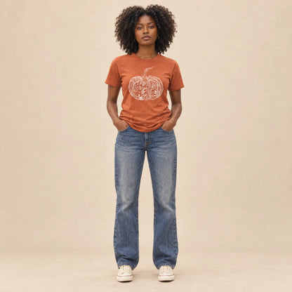 Full-length view of a woman in a heather autumn orange floral pumpkin graphic tee and straight leg jeans on a neutral backdrop