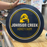 Custom Johnson Creek Honey Farm sign in dark blue and yellow being held by a person.