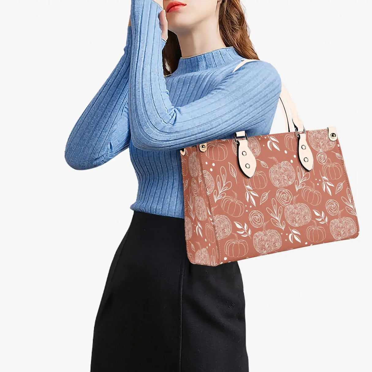 Woman wearing blue sweater holding Flower Pumpkin Luxury Handbag with intricate pumpkin pattern stylishly against white background