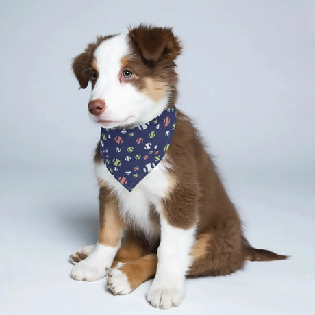 Puppy wearing a tennis ball patterned dog bandana, sitting on a white background.