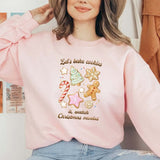 Pink sweatshirt featuring "Let's bake cookies & watch Christmas movies" with festive designs of cookies, candy canes, and decorations.