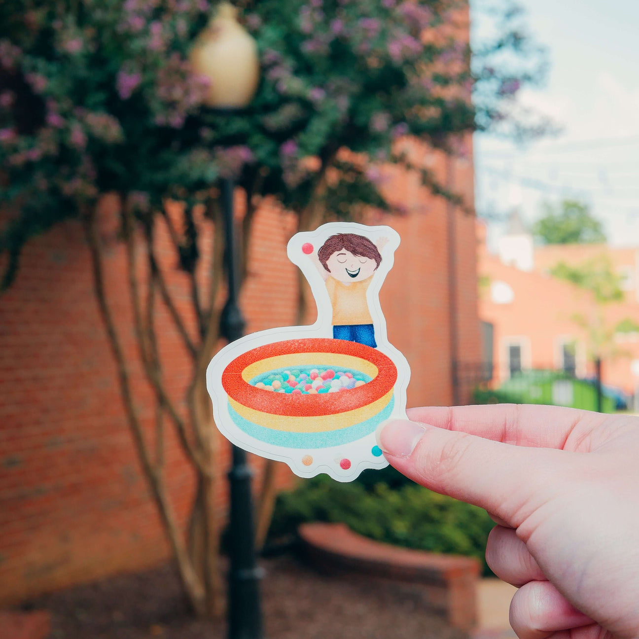 Hand holding Max's Festival Adventure Ball Pit sticker outdoors