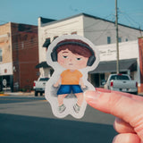 Person holding a Max's Festival Adventure sticker showing Max with headphones in a colorful town background.