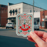 Hand holding NC Hot Sauce Contest & Festival sticker in front of downtown street