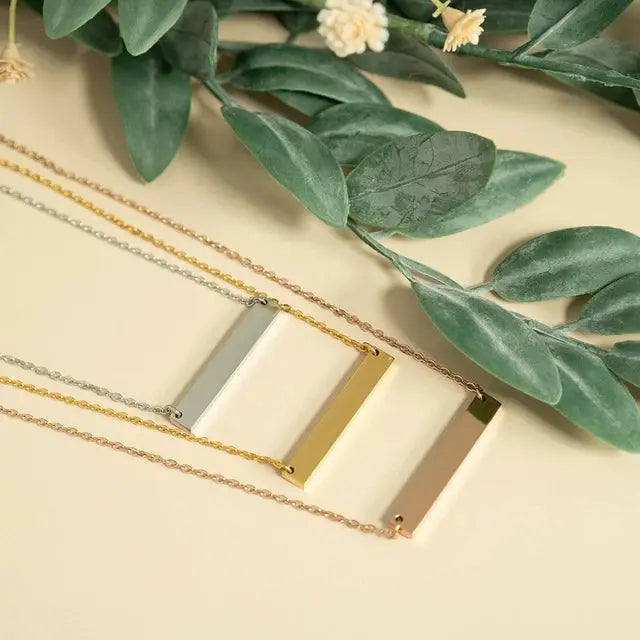 18K gold engraved bar necklace from Winks Design Studio, personalized stainless steel jewelry, close-up of sleek, modern pendant.