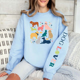 Woman wearing soft blue Dog Lover Crewneck with colorful dog illustrations and text on the sleeve.