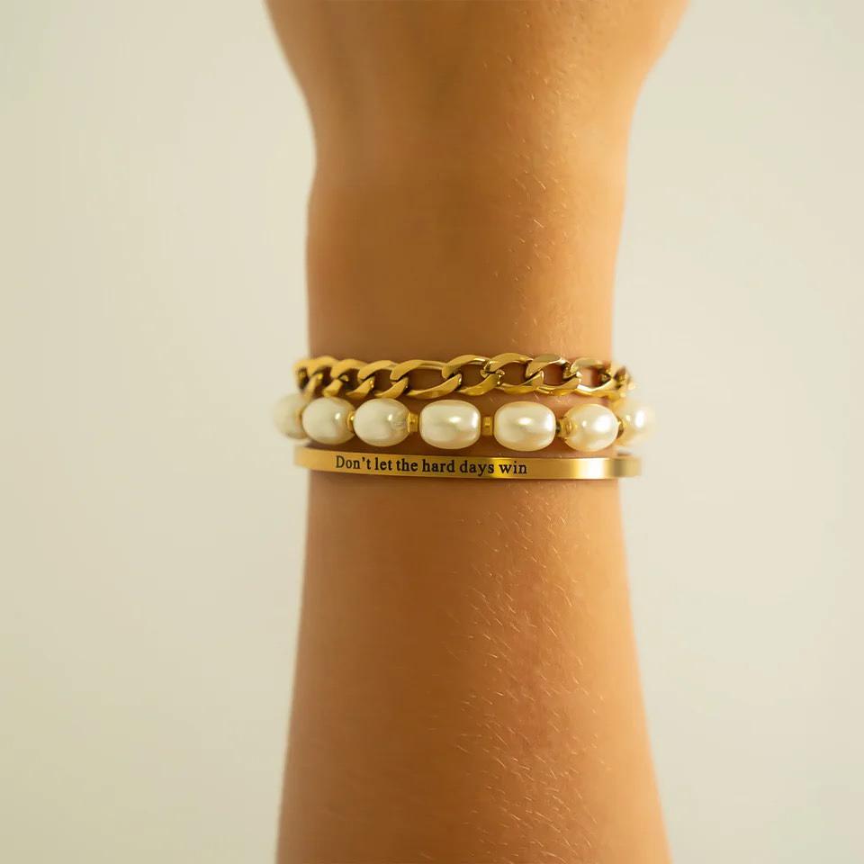 Gold bracelet with pearl accents and a motivational quote on a wrist against a neutral background