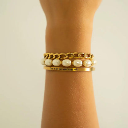 Gold bracelet with pearl accents and a motivational quote on a wrist against a neutral background