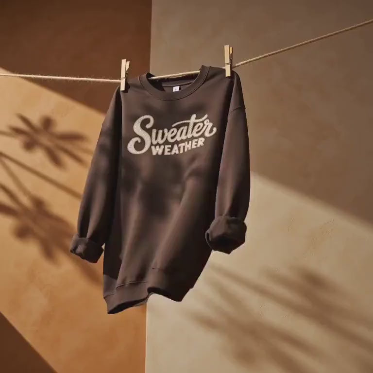 Dark chocolate brown "Sweater Weather" graphic crewneck sweatshirt hanging on a clothesline
