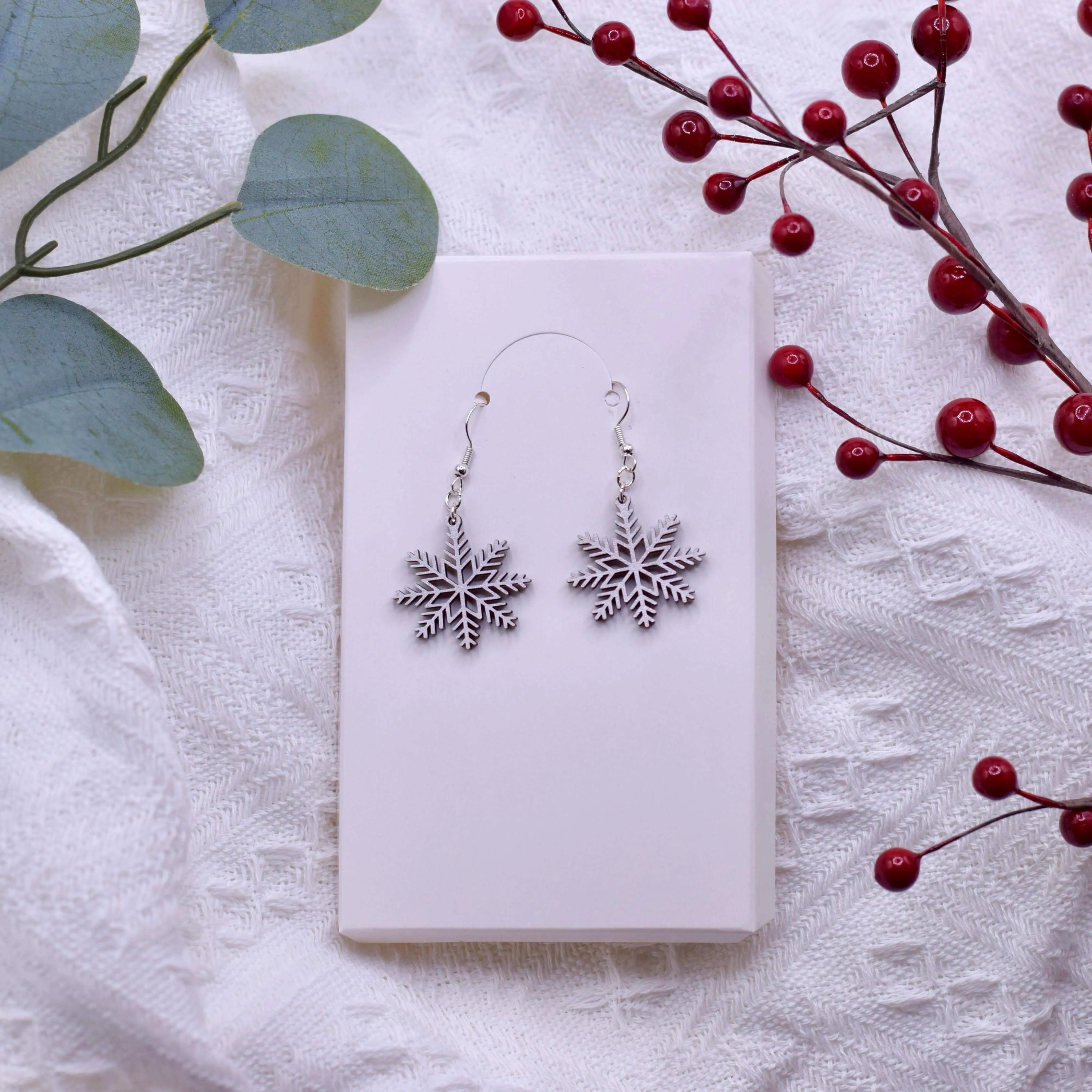 Wooden shimmering snowflake earrings by Winks Design Studio, LLC, featuring intricate snowflake design with a sparkling finish.