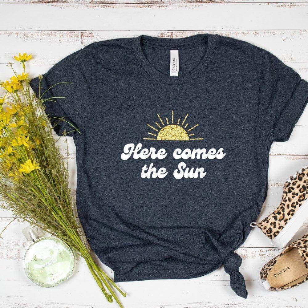Winks Design Studio LLC Here Comes The Sun T-shirt showing a bright sun graphic and casual fit, in a small size.