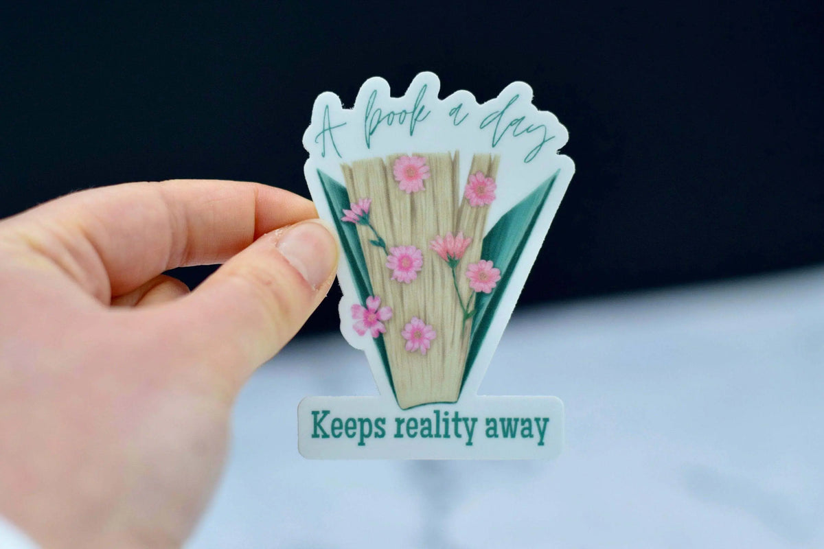Vinyl sticker from Winks Design Studio featuring the phrase "A Book a Day Keeps Reality Away" with book illustrations.